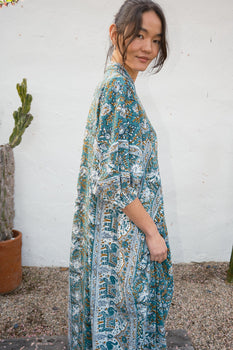 A woman standing outside by white door wearing a multi colored caftan