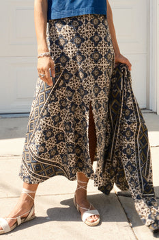 a woman standing by a fence wearing an ivory pleated blouse and tapestry print skirt.