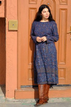 woman leaning on an orange door wearing a navy tapestry dress.