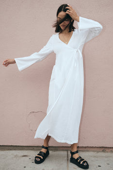 woman standing by pink wall wearing a white dress