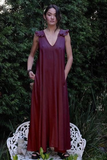 Woman in a black fig dress standing on a white chair with greenery in the background