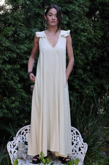 Woman wearing an alabaster dress standing on a white chair with greenery in the background