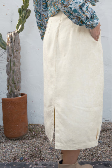 Person wearing an alabaster skirt standing next to a cactus plant against a white wall.