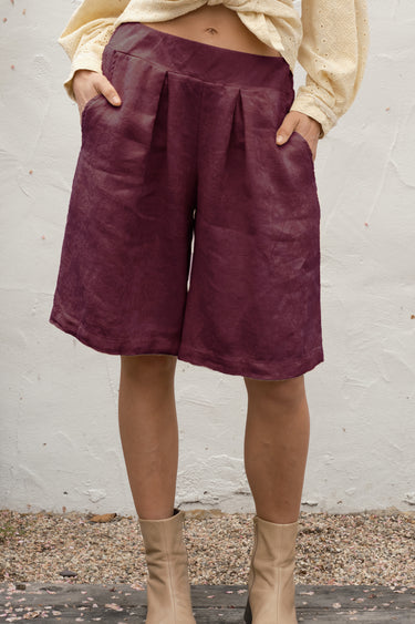 Person wearing black fig shorts and beige boots against a white wall.