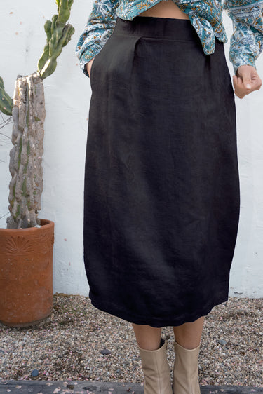 Person wearing a black skirt with a white wall and cactus plant in the background