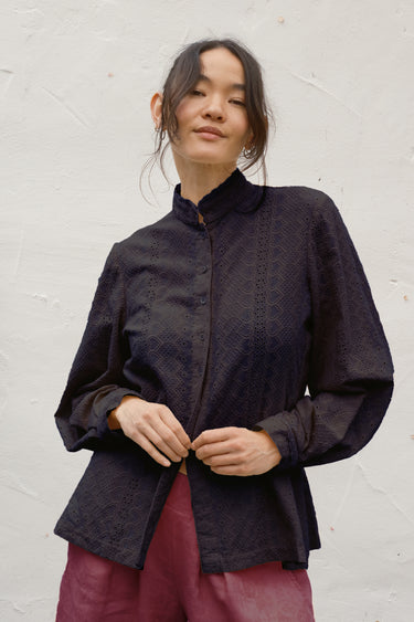 Person wearing a jet black blouse and red pants against a white background