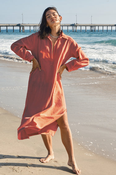 Woman in a persimmon dress standing on a beach with a pier in the background
