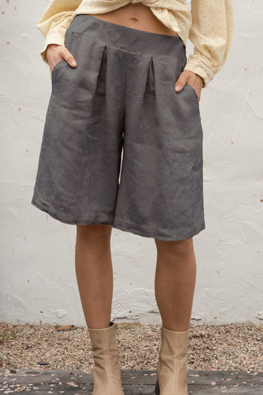 Person wearing gray shorts and beige boots against a white wall.