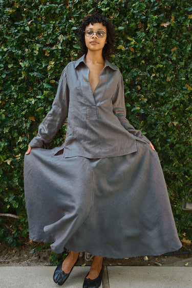 woman wearing pewter skirt and blouse standing in front of greenery