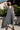 Woman wearing a gray sleeveless dress standing outdoors with greenery in the background