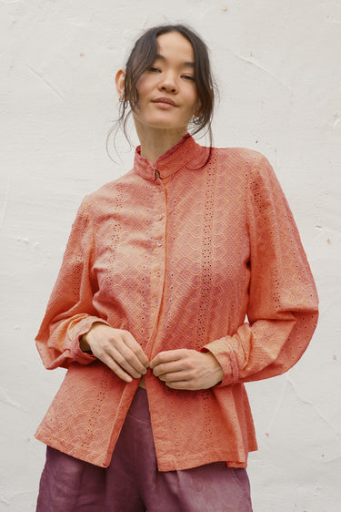 Woman wearing persimmon blouse with lace details against a white background