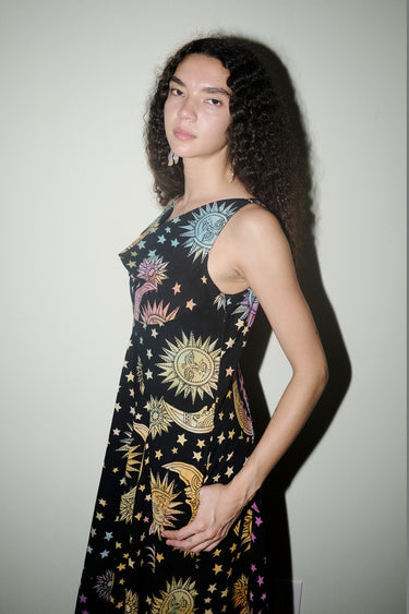 Woman wearing a black sleeveless dress with celestial pattern against a plain background