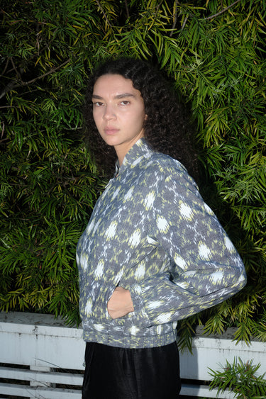 Woman outdoors wearing a gray with white and yellow ikat zip front jacket with black pants, side view.