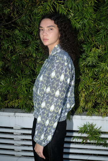Woman outdoors wearing a gray with white and yellow ikat zip front jacket with black pants, side view.