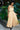 Woman in a long yellow dress standing outdoors with greenery around