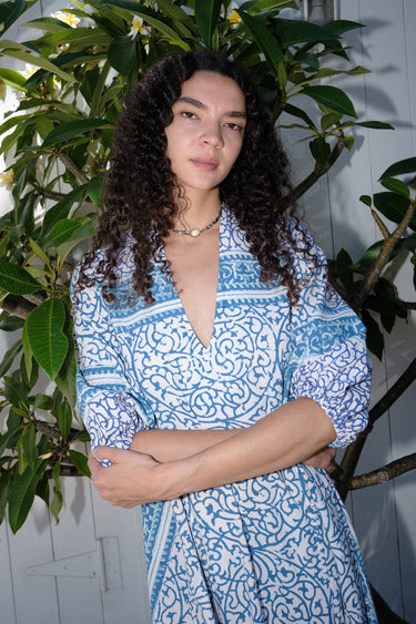 A woman standing outdoors wearing a blue and white patterned maxi dress with three quarter balloon sleeves and cell phone pockets.