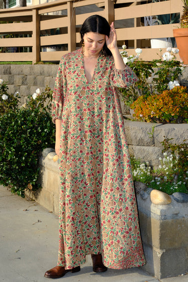 A woman standing outside wearing a beige ground with red and brown floral caftan.