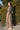 A woman wearing a maxi caftan with a floral pattern in a color that could be described as celadon green ground with tan, brown and blue, belted, standing outdoors.