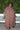 A woman outside standing against greenery wearing a raisin floral tapestry maxi caftan with three quarter balloon sleeves .