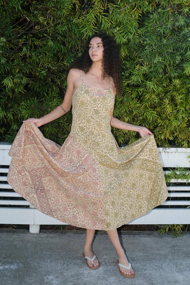 A woman wearing a mixed print slip dress of pea and blush calico tapestry, posing outdoors.
