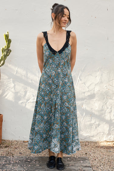 Woman wearing a floral dress with black lace details against a white wall.