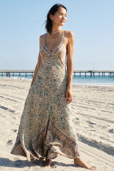 Woman in a floral dress standing on a beach with a pier in the background