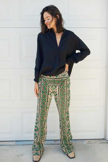 A person wearing a flare legged full length pant with a mid rise and a hand block printed Indian Tapestry design. worn with a black blouse