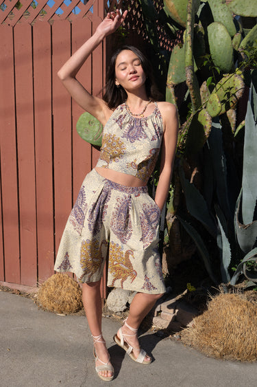 Woman in a patterned short set standing outdoors with plants and a wooden fence in the background