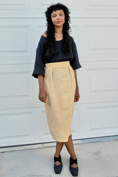 Woman wearing a black top and yellow skirt standing in front of a white garage door.