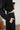 Person wearing a black outfit with a white wall and plant in the background