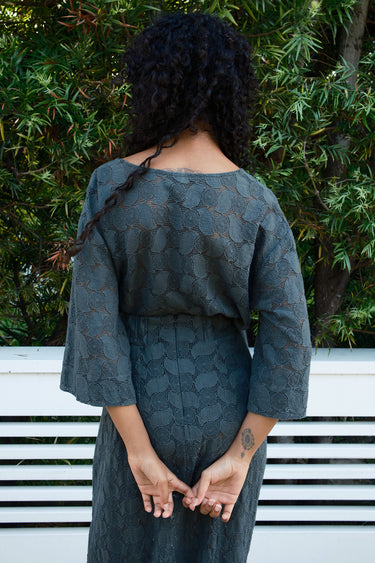 Person wearing a pewter gray lace patterned tee and skirt with a natural background