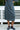 Person wearing a gray patterned lace skirt and black shoes standing in front of a white bench.