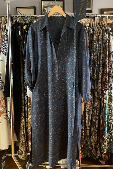 Blue patterned shirt on a hanger against a background of vintage clothing racks.