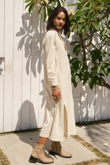 A woman standing outdoors wearing an alabaster midi shirt dress with long sleeves, paired with boots.