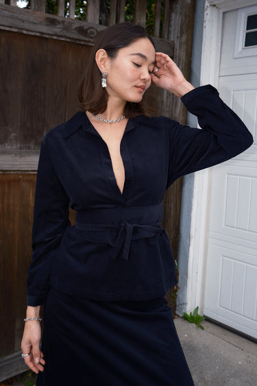 A woman wearing an ebony black corduroy shirt with long sleeves and an obi belt.
