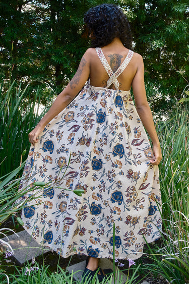 Woman wearing a floral dress standing in a natural setting with greenery.