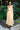 Woman in a light yellow dress standing in front of green plants