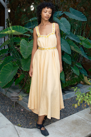 Woman in a light yellow dress standing in front of green plants