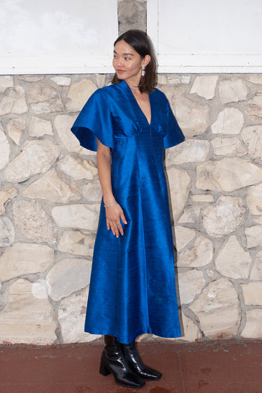 woman standing by stone wall wearing a sapphire blue zip front dress with black boots
