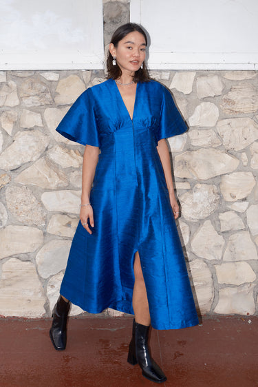 woman standing by stone wall wearing a sapphire blue zip front dress with black boots