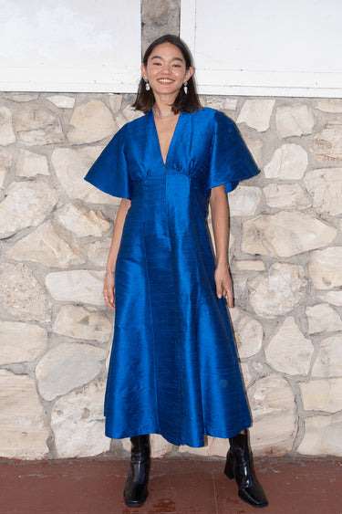 woman standing by stone wall wearing a sapphire blue zip front dress with black boots
