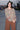 A woman standing at a beach boardwalk wearing a floral print tapestry blouse and a nutmeg brown trouser.