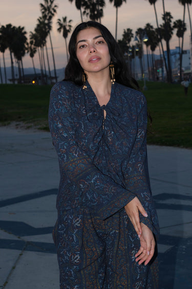 A woman standing at Venice Beach at dusk wearing dark blue midnight sky handloom tapestry shirt with bell sleeves.