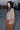 A woman standing at a beach boardwalk wearing a nutmeg brown trouser and a floral print blouse. Side View