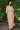 Woman wearing a tapestry top and pink skirt standing outdoors with greenery in the background