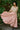 Woman in a gold top and pink skirt standing outdoors with greenery in the background