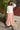 Woman wearing a white blouse and pink skirt standing outdoors.