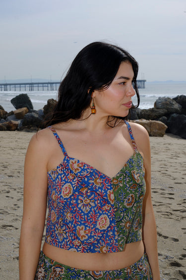 A woman standing at the beach wearing a floral tapestry camisole cut using both green and blue tapestry of the same print tapestry mixed together. Worn with matching pants.