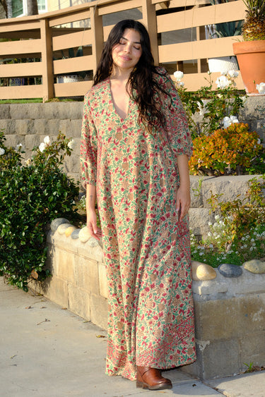 A woman standing outside wearing a beige ground with red and brown floral vintage rose tapestry caftan.