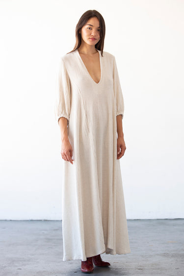 woman standing in photo studio wearing a maxi alabaster caftan with deep v neck and balloon sleeves